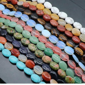 Può includere: Una varietà di perline ovali in pietre preziose di diversi colori, tra cui turchese, verde, rosso e nero. Le perline sono disposte in file, creando uno schema colorato e testurizzato.