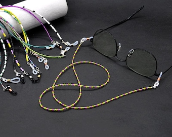 Puede incluir: Una colección de cadenas de gafas con cuentas de varios colores, incluyendo verde, morado y amarillo. Un par de gafas con montura negra está unido a una cadena. Las cadenas están diseñadas para sujetar gafas.