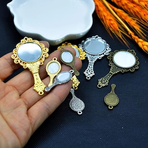 以下が含まれることがあります： 金、銀、ブロンズなど、さまざまな金属仕上げの小さな装飾的な手鏡のコレクション。鏡は装飾的なフレームと、小さく丸いまたは楕円形の反射面を持っています。ジュエリーやその他の工芸品に取り付けるためのループが付いているものもあります。