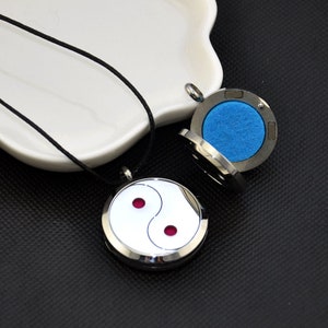 May include: A silver yin yang aromatherapy diffuser necklace with a black cord. The diffuser is open, revealing a blue felt pad inside.