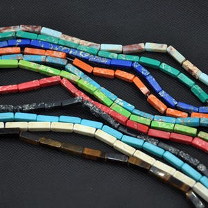 May include: A selection of colourful, rectangular gemstone beads in shades of blue, green, red, orange, and brown. The beads are strung together, creating a textured and vibrant display, ideal for jewellery making.