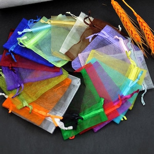 May include: A collection of small, colorful organza gift bags in various shades, including blue, green, orange, and purple. Each bag is tied with a matching ribbon drawstring. The bags are arranged in a circular pattern.