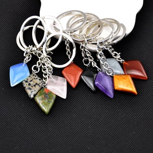May include: A set of ten gemstone keychains with silver key rings and chains. The gemstones are in various colors, including red, orange, yellow, green, blue, purple, and black. The gemstones are all cut into a diamond shape.