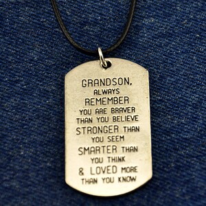 May include: Silver dog tag necklace with a black cord. The dog tag has an inspirational message for a grandson: "Grandson, Always Remember You Are Braver Than You Believe Stronger Than You Seem Smarter Than You Think & Loved More Than You Know"