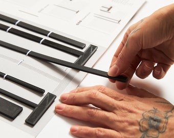 May include: A person is assembling black plastic T-shaped pieces on a white surface with a diagram of the pieces.