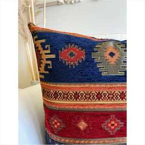 May include: A blue, red, and orange patterned throw pillow with a geometric design. The pillow has a woven texture and is made of a soft, comfortable fabric.