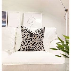 Puede incluir: Un sof&aacute; blanco con un coj&iacute;n de estampado de leopardo en color beige y negro. El sof&aacute; est&aacute; en una habitaci&oacute;n con paredes blancas y un dibujo enmarcado de una cabeza de caballo.