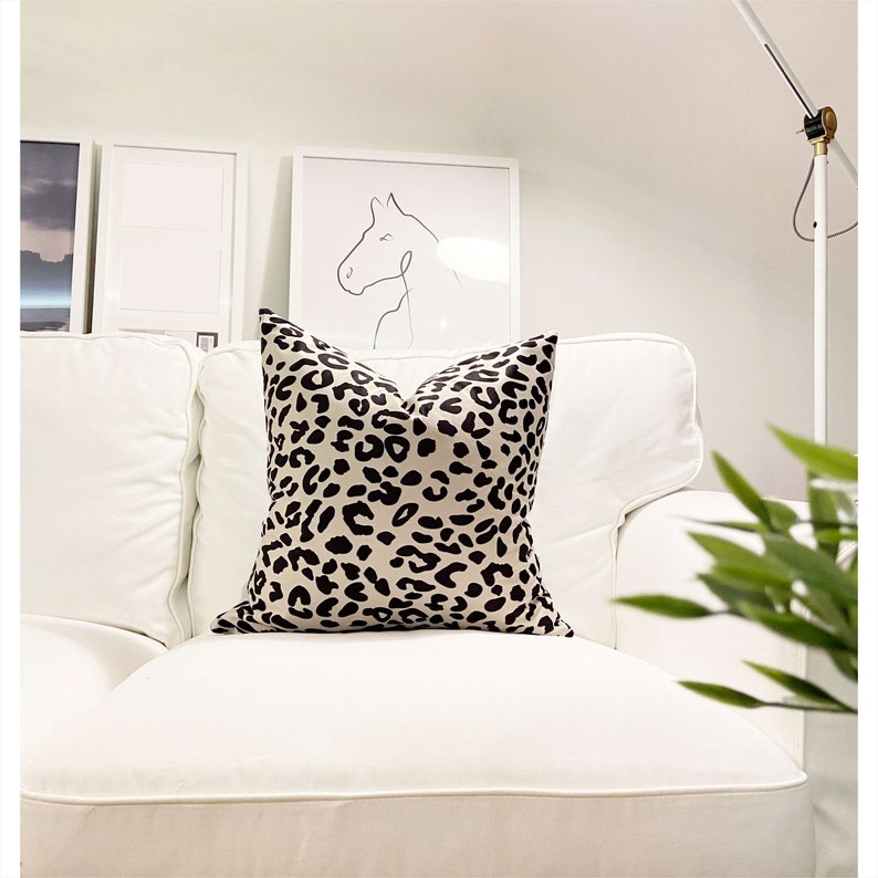 Puede incluir: Un sof&aacute; blanco con un coj&iacute;n de estampado de leopardo en color beige y negro. El sof&aacute; est&aacute; en una habitaci&oacute;n con paredes blancas y un dibujo enmarcado de una cabeza de caballo.
