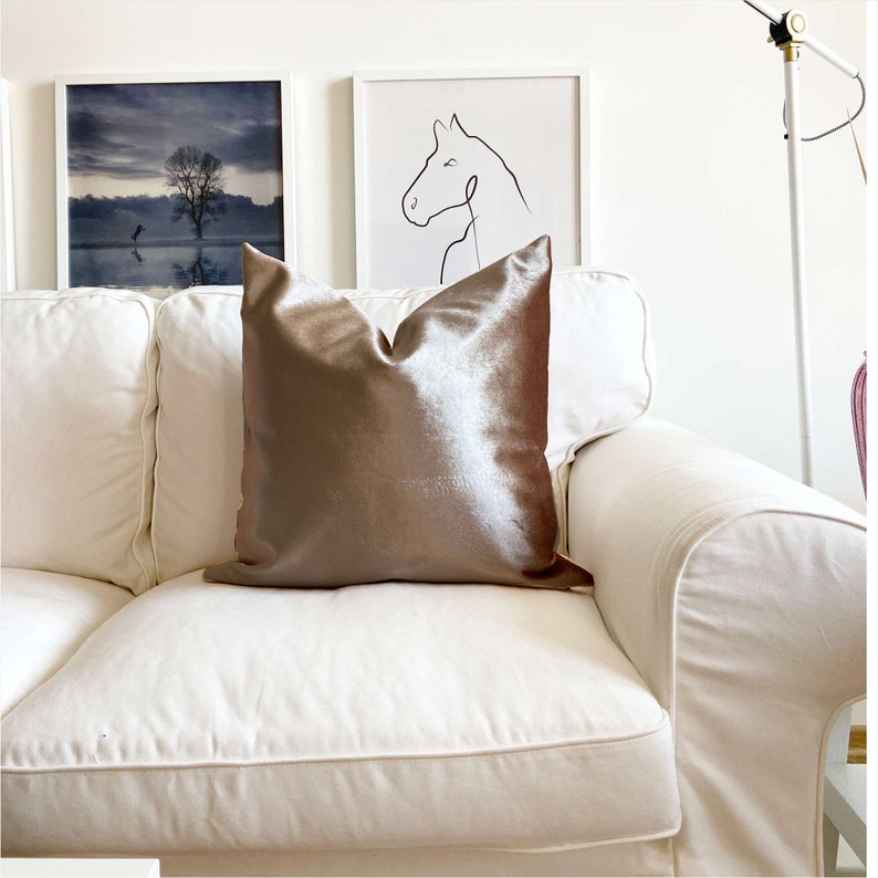 May include: A white couch with a brown velvet pillow. The couch is in a living room with two framed pictures on the wall behind it.