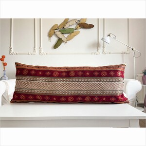 May include: A long, rectangular pillow with a red, white, and brown geometric pattern. The pillow is made of a soft, woven fabric and has a fringe trim.
