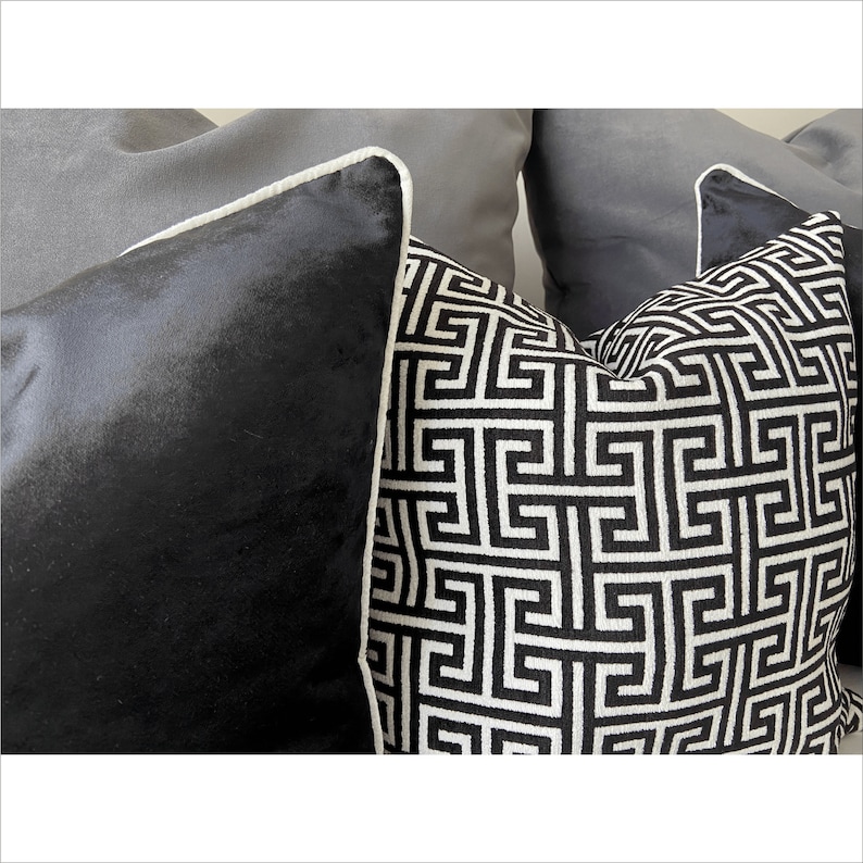 May include: Two decorative throw pillows with a black and white geometric pattern. One pillow is black velvet with a white trim. The other pillow has a white trim and a black and white geometric pattern.