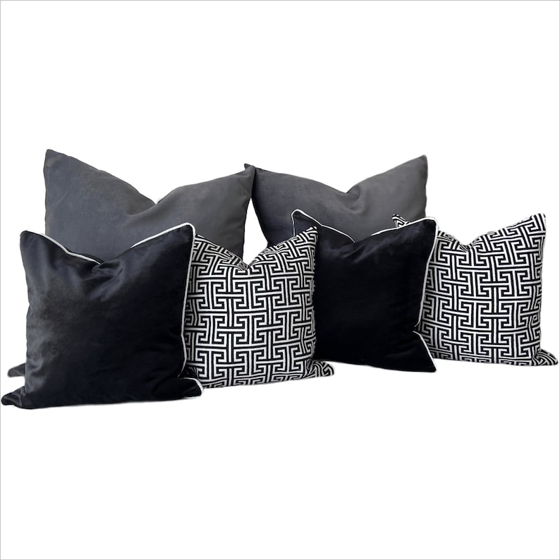 May include: A set of five decorative throw pillows. Two pillows are black velvet with white piping. Three pillows are black and white geometric patterned with white piping.