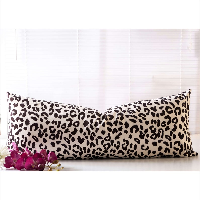Puede incluir: Una almohada larga y rectangular con fondo blanco y estampado de leopardo negro. La almohada est&aacute; sobre una superficie blanca.