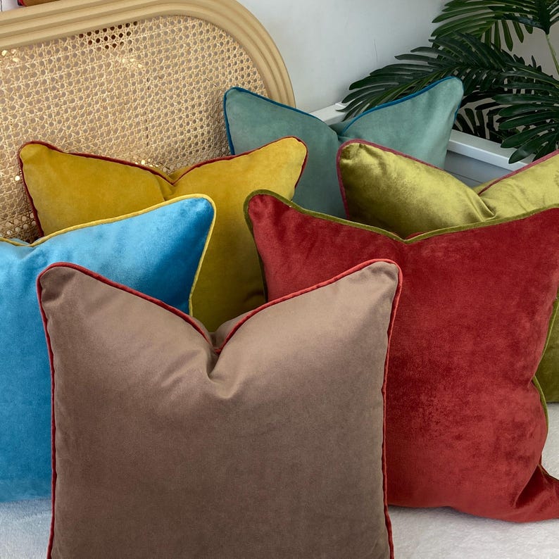 May include: A collection of six velvet throw pillows with contrasting colored piping. The pillows are in shades of mustard yellow, teal, olive green, brown, and red.