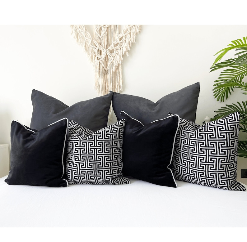 May include: Five throw pillows on a white couch. Two pillows are black velvet, two are black and white geometric patterned, and one is a solid charcoal gray.