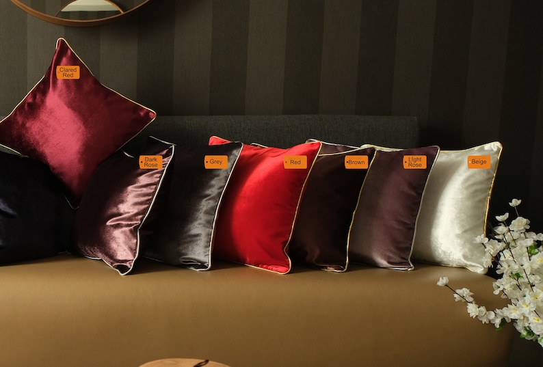 Puede incluir: Ocho cojines decorativos con diferentes colores y texturas. Los cojines est&aacute;n dispuestos en una fila en un sof&aacute; marr&oacute;n. Los colores de los cojines son: granate, rosa oscuro, gris, rojo, marr&oacute;n, rosa claro y beige.
