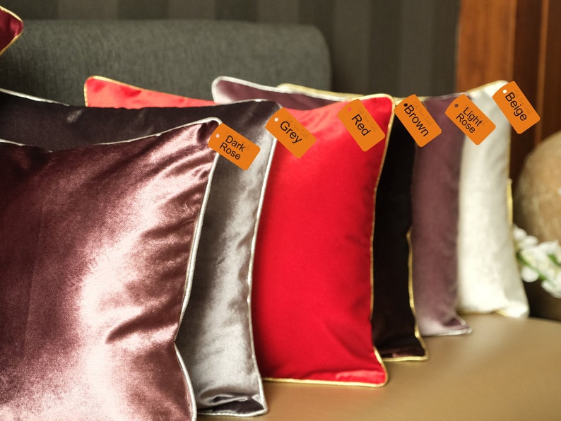 Puede incluir: Un conjunto de cojines decorativos en varios colores, incluyendo beige, rosa claro, marr&oacute;n, rojo, gris y rosa oscuro. Los cojines tienen un ribete blanco y est&aacute;n dispuestos en una fila en un sof&aacute;.