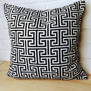 May include: Black and white geometric patterned throw pillow with a square design. The pillow is made of a soft, woven fabric.