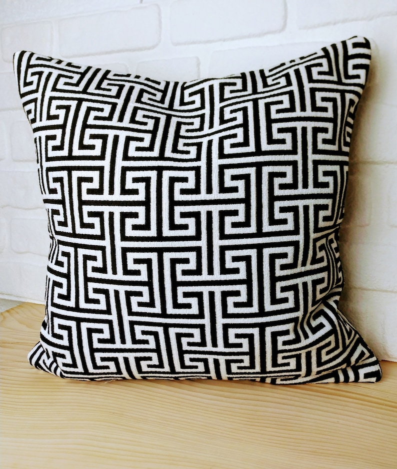 May include: Black and white geometric patterned throw pillow with a square design. The pillow is made of a soft, woven fabric.
