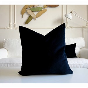 May include: A black velvet pillow on a white couch. The pillow is square and has a smooth, soft texture.