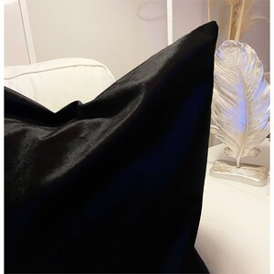 May include: A black velvet pillow with a smooth, soft texture. The pillow is folded in half and appears to be made of high-quality fabric.