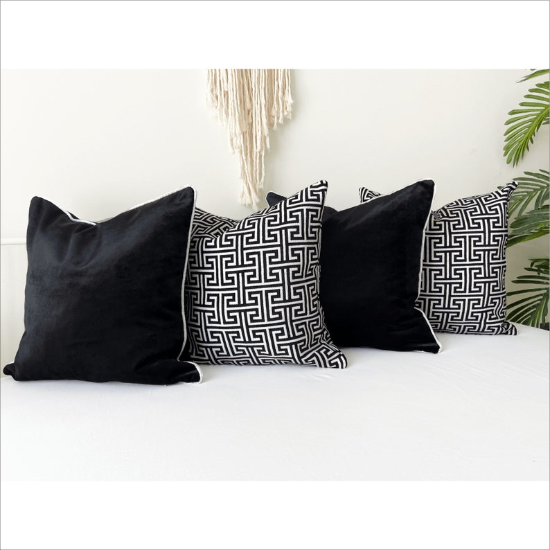 May include: Four decorative throw pillows, two black velvet and two with a white and black geometric pattern. The pillows are arranged on a white couch.