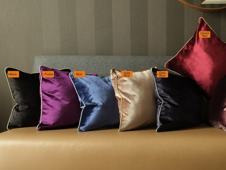 Puede incluir: Seis cojines decorativos de diferentes colores y texturas. Los cojines est&aacute;n dispuestos en una fila en un sof&aacute; marr&oacute;n. Los colores de los cojines son negro, morado, azul, vis&oacute;n dorado, azul oscuro y rojo oscuro.