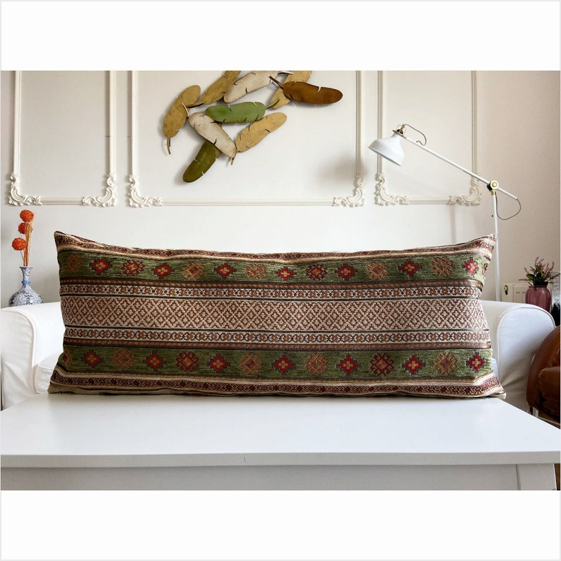 May include: A long, rectangular pillow with a green, red, and cream patterned fabric. The pillow has a geometric design with stripes and diamonds.