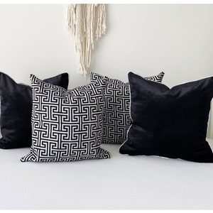 May include: Four decorative throw pillows, two with a black and white geometric pattern and two solid black velvet. The pillows have white piping around the edges.