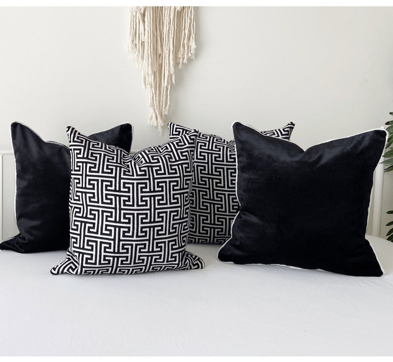 May include: Four decorative throw pillows, two with a black and white geometric pattern and two solid black velvet. The pillows have white piping around the edges.