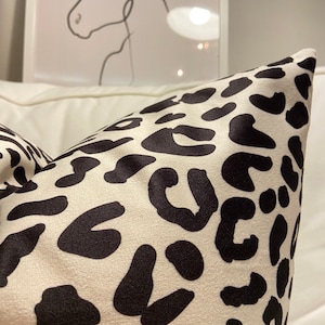 Puede incluir: Una almohada blanca con un estampado de leopardo negro.