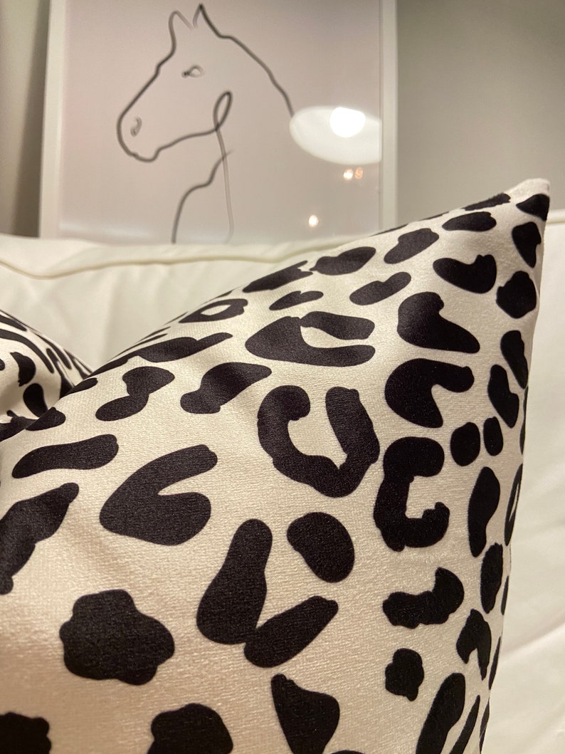 Puede incluir: Una almohada blanca con un estampado de leopardo negro.