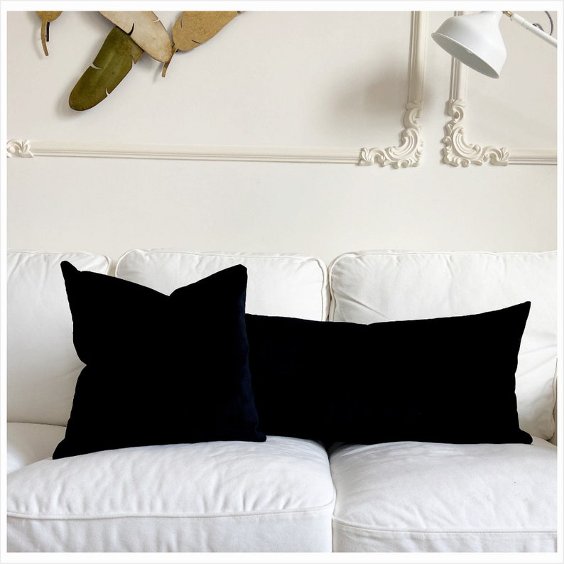 May include: Two black velvet throw pillows on a white couch. The pillows are square and rectangular in shape.