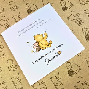 May include: A white card with a Winnie the Pooh illustration and the text "Sometimes the smallest things take up the most room in your heart - A.A. Milne, Winnie the Pooh."  The card also has the text "Congratulations on becoming a Grandad" with a small wooden heart.