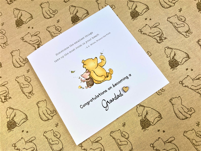 May include: A white card with a Winnie the Pooh illustration and the text "Sometimes the smallest things take up the most room in your heart - A.A. Milne, Winnie the Pooh."  The card also has the text "Congratulations on becoming a Grandad" with a small wooden heart.