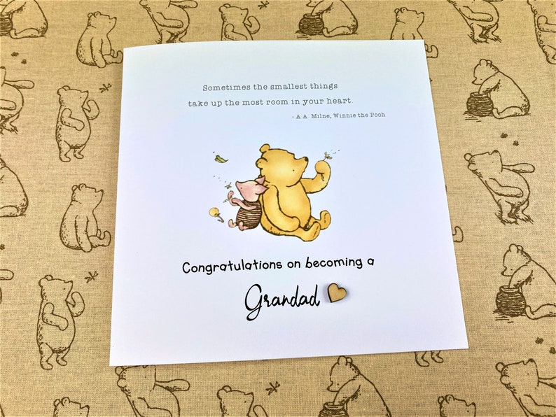 May include: A Winnie the Pooh and Piglet illustration on a white card with the text "Sometimes the smallest things take up the most room in your heart - A.A. Milne, Winnie the Pooh" and "Congratulations on becoming a Grandad".