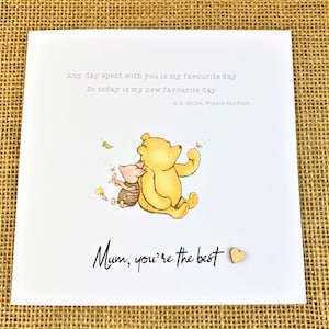 May include: A greeting card with a Winnie the Pooh illustration. The image features Pooh Bear and Piglet, with the text "Mum, you're the best." and a quote by A.A. Milne. A small wooden heart is attached to the card.