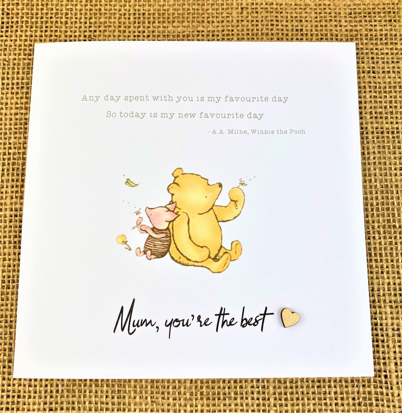 May include: A greeting card with a Winnie the Pooh illustration. The image features Pooh Bear and Piglet, with the text "Mum, you're the best." and a quote by A.A. Milne. A small wooden heart is attached to the card.