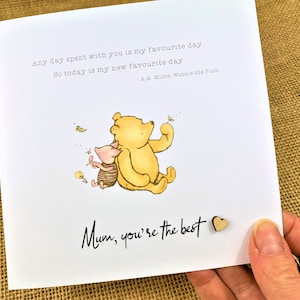 May include: A greeting card featuring Winnie the Pooh and Piglet. The card has the text "Any day spent with you is my favourite day. So today is my new favourite day - A.A. Milne, Winnie the Pooh." and "Mum, you're the best."