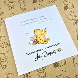 May include: A Winnie the Pooh and Piglet card with a quote from A.A. Milne. The card is white with a blue background for the illustration. The card says "Congratulations on becoming an Any Recipient".