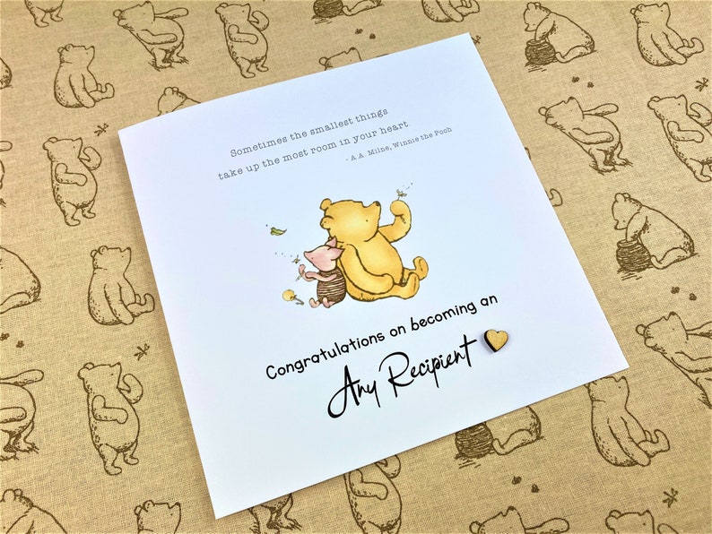 May include: A Winnie the Pooh and Piglet card with a quote from A.A. Milne. The card is white with a blue background for the illustration. The card says "Congratulations on becoming an Any Recipient".