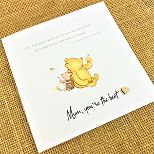 May include: A white greeting card featuring a watercolor illustration of Winnie the Pooh and Piglet. The card includes the text "Any day spent with you is my favourite day. So today is my new favourite day" and "Mum, you're the best."