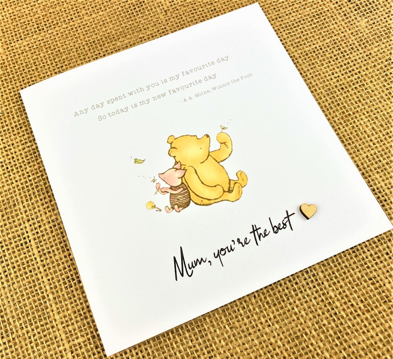 May include: A white greeting card featuring a watercolor illustration of Winnie the Pooh and Piglet. The card includes the text "Any day spent with you is my favourite day. So today is my new favourite day" and "Mum, you're the best."