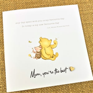 May include: A white greeting card featuring a watercolor illustration of Winnie the Pooh and Piglet. The card includes the text "Any day spent with you is my favourite day. So today is my new favourite day." and "Mum, you're the best."