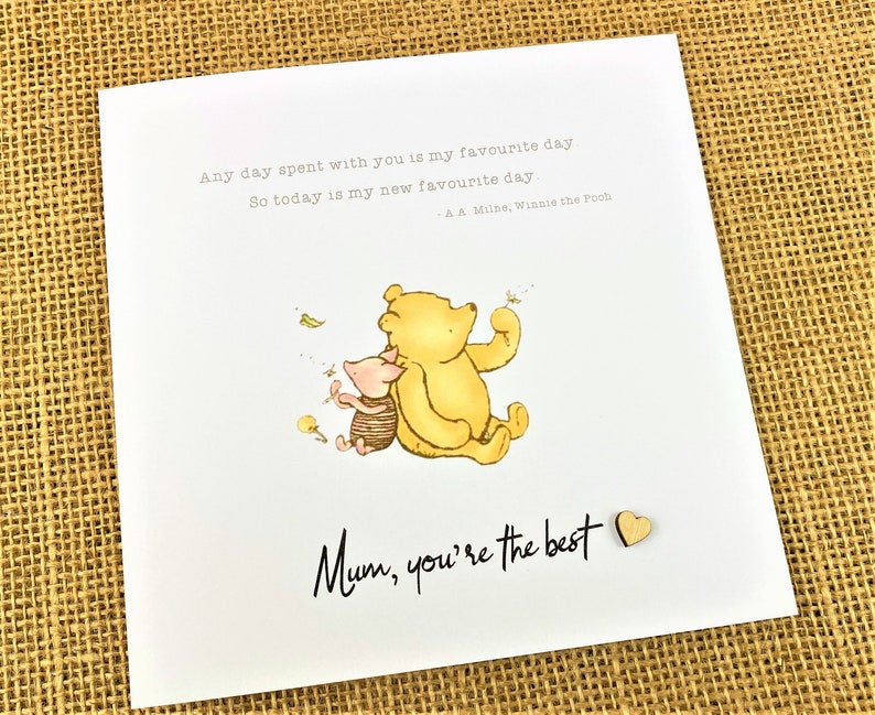 May include: A white greeting card featuring a watercolor illustration of Winnie the Pooh and Piglet. The card includes the text "Any day spent with you is my favourite day. So today is my new favourite day." and "Mum, you're the best."