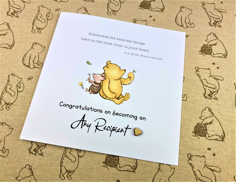 May include: A white card with a Winnie the Pooh and Piglet illustration. The card has the text "Sometimes the smallest things take up the most room in your heart - A A Milne, Winnie the Pooh" and "Congratulations on becoming an Any Recipient".