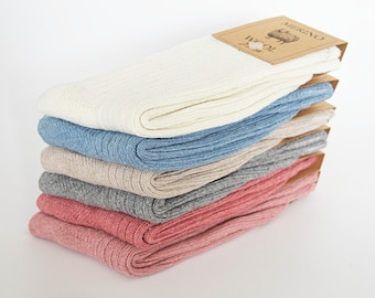 May include: A stack of six pairs of ribbed merino wool socks in various colors: white, light blue, beige, gray, and two shades of pink. Each pair is folded and has a brown paper label with the word "MERINO WOOL".