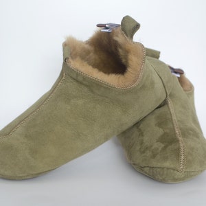 Può includere: Un paio di pantofole in pelle scamosciata verde con fodera in pelliccia sintetica. Le pantofole hanno una punta a punta e un retro chiuso.