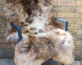May include: A brown and white sheepskin rug draped over a black plastic chair. The rug has a long, soft pile and is ideal for adding warmth and comfort to any room.