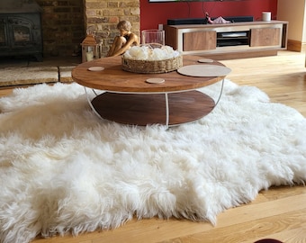 May include: A white fluffy sheepskin rug with a round wooden coffee table with a white metal frame. The table has a white ceramic coaster and a woven basket with white flowers.